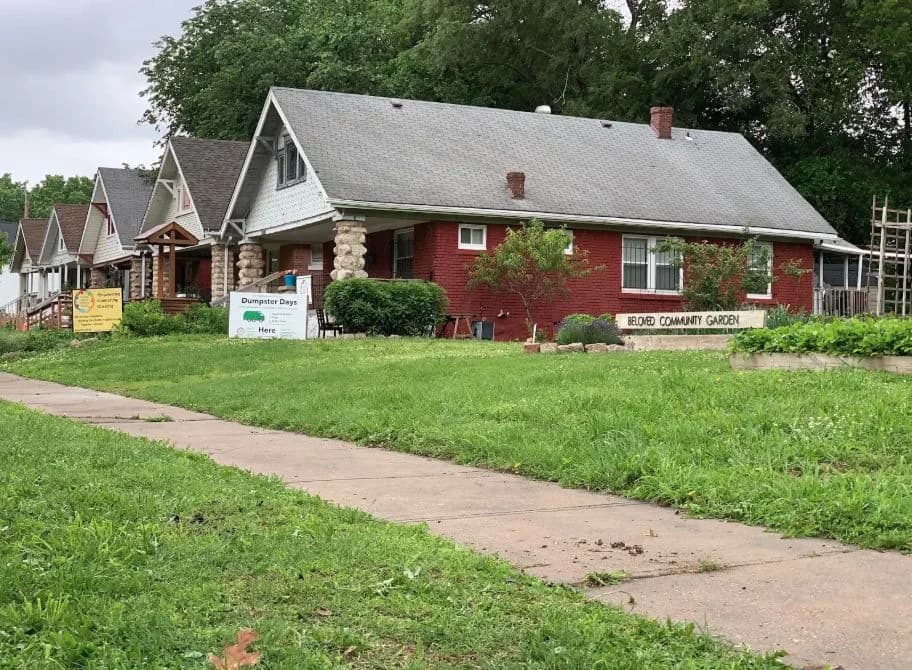 The same residential curb and community-garden frontage after the stack of used tires was removed.